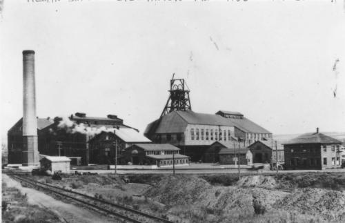 A black and white photograph of at least 8 buildings and a large smokestack of the Allan Shaft of the Acadia Coal Company.