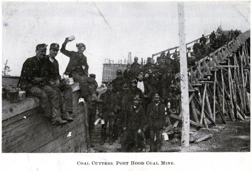 A group of miners near the slope opening of a mine, several holding lunch cans (known as piece cans) and water canteens, with open-flame bicket lights on their caps, circa 1909.]