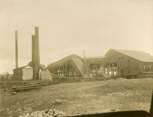 Sepia-coloured photograph showing surface buildings and smokestacks of a coal mine, including the covered slope into the mine. This is the Cumberland Railway & Coal Company Colliery, West Slope, Springhill, Cumberland County. Burke W. Weston? photographer. Nova Scotia Museum: P119.118. 