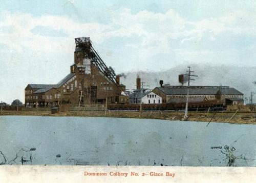 : Postcard of the surface buildings of No. 2 Colliery in Glace Bay, 1912. There is a pond in the foreground and smoke coming from a chimney. The bankhead is featured prominently.