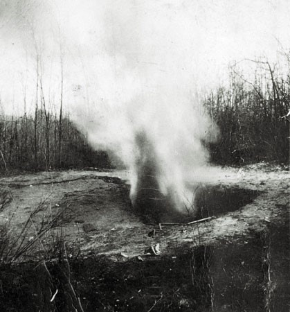 : A black and white photograph showing a small  explosive cloud near ground level. It is said that this was methane gas spontaneously escaping from the ground in Pictou County.