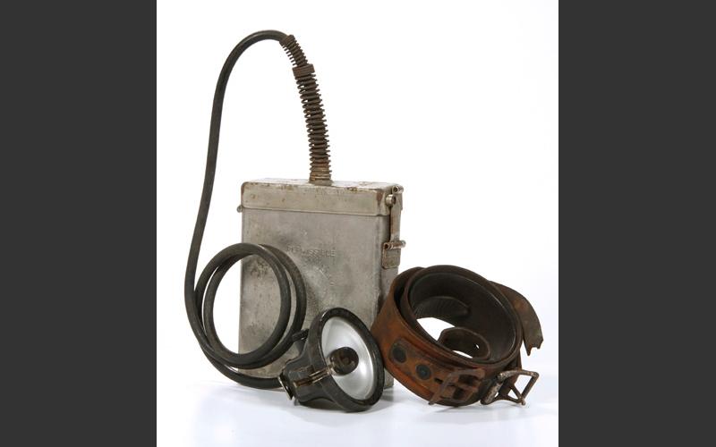 Electric head lamp with battery pack and leather belt. These became standard equipment in the postwar years and are still in use in modern mines. The lamp hooks onto the front of the miner’s hardhat.
