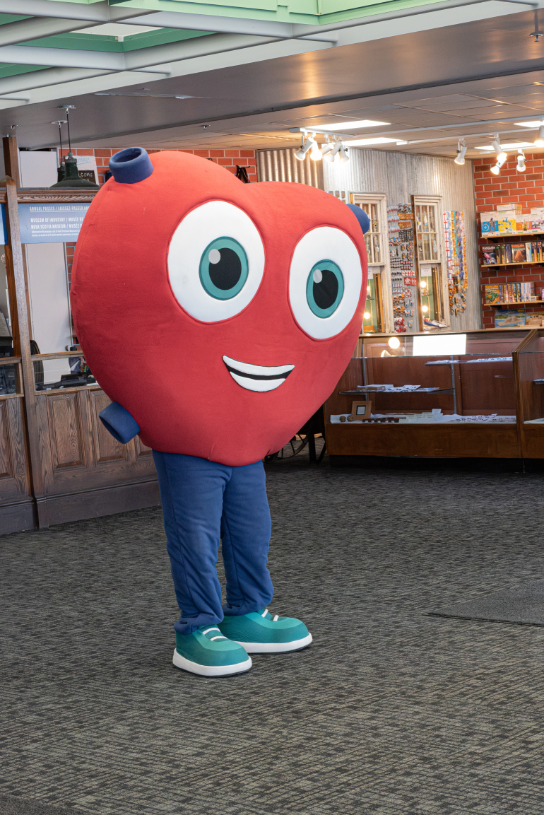 Heart mascot standing in the Museum of Industry lobby wearing blue pants and teal shoes